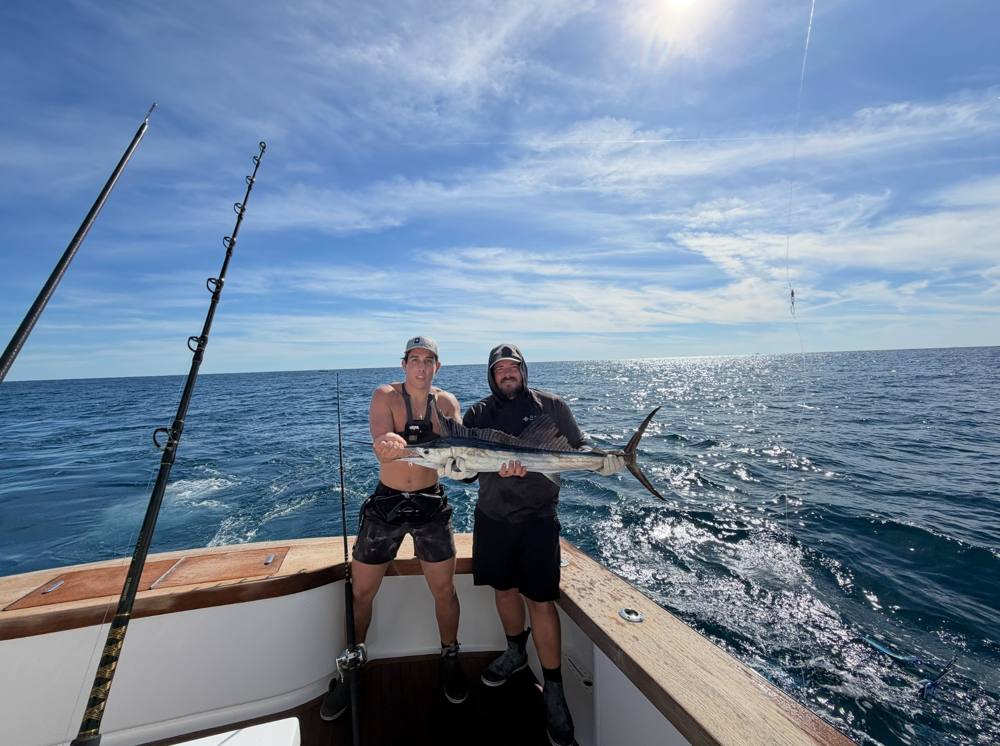 Two anglers holding a wahoo in the cockpit offshore
